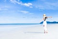Asian woman, long black hair, wore white dress and hat sitting on the beach near the woven bags and sunglasses and facing back by Royalty Free Stock Photo