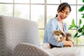 Asian woman look fun with fluffy cat that look at camera with confuse face and they stay on sofa in living room with day light