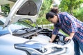 Asian woman looking and check under the hood of broken down car on the side of the road Royalty Free Stock Photo