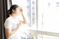 Asian woman looking out window at strong sunlight,hot weather,high temperature heat wave,harsh ultraviolet rays of sun,risk of