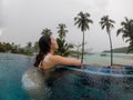 Asian woman in luxury swimming pool looking away to the ocean in rainy day. travel bad weather concept. Royalty Free Stock Photo
