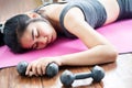 Asian woman lying down on floor feeling tired after doing sport, overtraining hand holding dumbbell