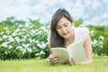 Asian woman lying on grass field for reading a white book in the park Royalty Free Stock Photo