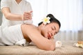 Asian woman lying on spa massage table, eyes closed, getting herbal ball stamp on her back