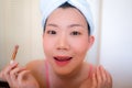 Asian woman and makeup - young happy and beautiful Chinese girl with towel head wrap with applying eye shadow looking at bathroom Royalty Free Stock Photo