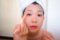 Asian woman and makeup - young happy and beautiful Korean girl with towel head wrap with applying eye shadow looking at bathroom Royalty Free Stock Photo