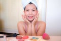 Asian woman and makeup - young happy and beautiful Korean girl with towel head wrap smiling cheerful at bathroom mirror preparing Royalty Free Stock Photo