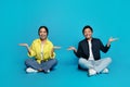 An Asian woman and man are sitting cross-legged on the floor with hands raised in a shrugging pose Royalty Free Stock Photo