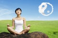 Asian woman meditating outdoors on the rock at meadow with yin yang clouds symbol in the sky Royalty Free Stock Photo