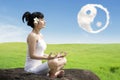 Asian woman meditating outdoors on the rock at meadow with yin yang clouds symbol in the sky Royalty Free Stock Photo