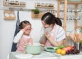 Asian woman mother and daughter play together in kitchen,mom hold tablet for teach little girl how to cook in semester break,