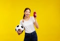 Asian woman over isolated yellow background holding a soccer ball and drink, sport concept Royalty Free Stock Photo