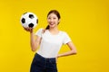 Asian woman over isolated yellow background, looking at camera and holding a soccer ball, sport concept Royalty Free Stock Photo
