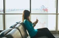 Asian woman passenger holding passport and checking flight or online check in and travel planner at airport