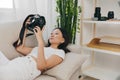 Asian woman photographer lying at home on couch and looking at photos in camera, freelance photographer work for self Royalty Free Stock Photo