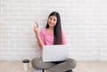 Asian woman in pink casual cloth holding credit card look at camera and using laptop to shopping online with bag at white brick Royalty Free Stock Photo