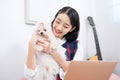 An Asian woman playing with a Maltese dog in a living room with a guitar and a laptop Royalty Free Stock Photo