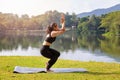 Asian woman practicing yoga doing Eagle Pose pose on the mat beside a lake in outdoor park