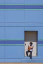 Asian woman in protective mask using smartphone in front of side entrance door of modern blue building in minimal style Royalty Free Stock Photo