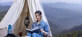Asian woman reading book while on a solo trekking camp on the top of the mountain with small tent for weekend activities and