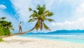 Asian woman relaxing at a coconut palm tree on a white tropical beach at La Digue Seychelles Islands