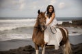 Asian woman riding horse on the beach. Outdoor activities. Woman wearing long white dress. Traveling concept. Cloudy sky. Copy Royalty Free Stock Photo