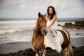 Asian woman riding horse on the beach. Outdoor activities. Woman wearing long white dress. Traveling concept. Cloudy sky. Copy Royalty Free Stock Photo