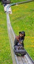 Asian woman riding summer toboggan sled down a hill through the beautiful flower meadow in Oeschinensee, Kandersteg, Switzerland