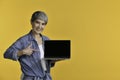 Asian woman 50s holding laptop computer and pointing fingers isolated on yellow background Royalty Free Stock Photo