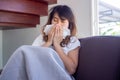 Asian woman sat ill on the sofa in the house, having fever, coughing, sneezing, and stuffy nose. Covering the nose with a piece of Royalty Free Stock Photo