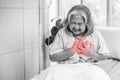 Asian woman seated on a hospital bed, clutching her chest with a pained expression