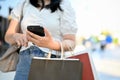 Asian woman with shopping bags using her smartphone, standing in front of shopping mall Royalty Free Stock Photo