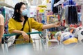 Asian woman with shopping cart wearing protective mask walking and buying at supermarket