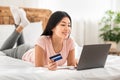 Asian Woman Shopping Online Using Laptop Lying On Bed Indoor Royalty Free Stock Photo