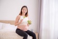 An Asian woman sits in her bedroom eating healthy, organic salads while she is pregnant until the time of her baby& x27;s birth