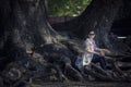 Asian woman sitting on big rain tree root in traveling destinati