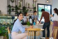 Asian woman sitting in cafe and feeling happy while she drink coffee and another people queue order beverage with barista