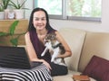 Asian woman sitting on couch in living room with  computer notebook  holding  Chihuahua dog  , looking and smiling at camera , Royalty Free Stock Photo