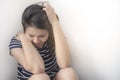 Asian woman is sitting disappointed on floor and looking down between legs with white background.