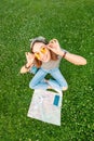 Asian woman sitting on grass in park with open map and smartphone and airplane toy. Tourism and travel concept