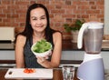 Asian woman sitting in kitchen  preparing healthy smoothie , holding bowl of gree vegetable in her hand smiling to camera Royalty Free Stock Photo