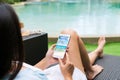 Asian woman sitting by the pool while using mobile phone. Female using travel application for flight tickets and hotel room online Royalty Free Stock Photo