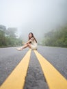 Asian woman sitting on road center line. road on mountain in foggy day.