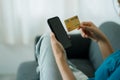 Asian woman sitting on a sofa holding a credit card to pay via smartphone Royalty Free Stock Photo