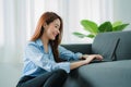 Asian woman sitting on sofa at home using digital tablet for work or online shopping. Touch screen freelance device for business o Royalty Free Stock Photo