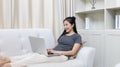 Asian woman sitting on sofa and using laptop to shop online with credit card to register for payment or online transactions Royalty Free Stock Photo