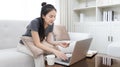 Asian woman sitting on sofa and using laptop to shop online with credit card to register for payment or online transactions Royalty Free Stock Photo
