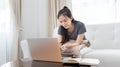 Asian woman sitting on sofa and using laptop to shop online with credit card to register for payment or online transactions Royalty Free Stock Photo