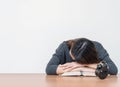 Asian woman sleep by lied on desk after she tired from reading book on blurred brown wooden desk and white cement wall textured ba Royalty Free Stock Photo