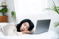 Asian woman sleeping in front of laptop lying in bed feeling tired from hard work Royalty Free Stock Photo